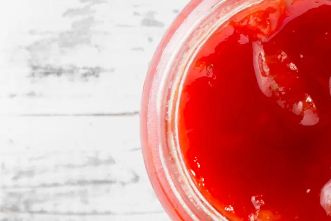 Close-up view of a jar of rich, glossy strawberry hot sauce with a vibrant red color, highlighting its smooth texture and perfect consistency for adding a sweet, spicy kick.