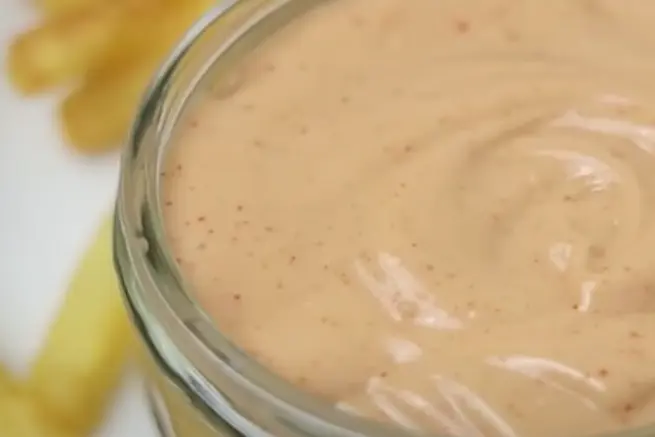 Close-up view of Zaxby’s Tongue Torch Sauce in a glass bowl, showcasing its creamy texture with a swirl, served alongside crispy French fries, ideal for dipping.