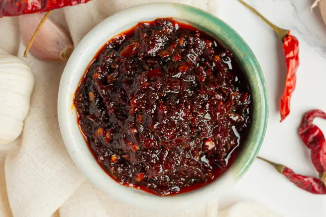 Close-up of crunchy shallot and garlic chili oil in a ceramic bowl, showcasing its rich texture and deep red color
