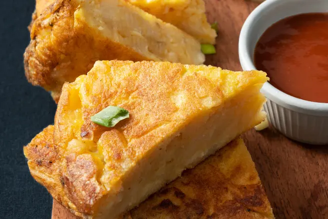 Golden, crispy slice of White Lily cornbread served with spicy dipping sauce on a wooden board