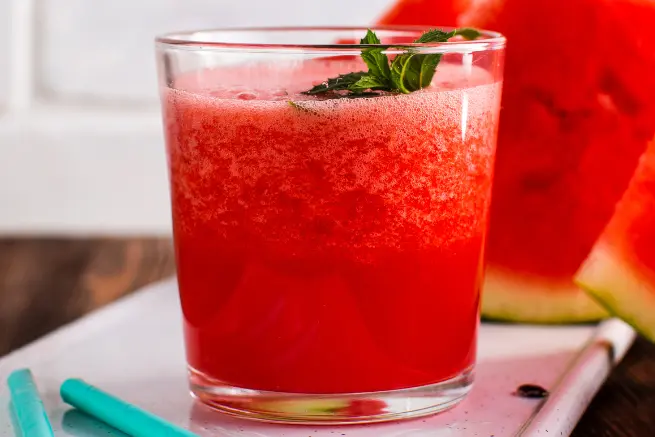 Close-up of a vibrant red watermelon shot with mint leaves in a glass, placed beside watermelon slices