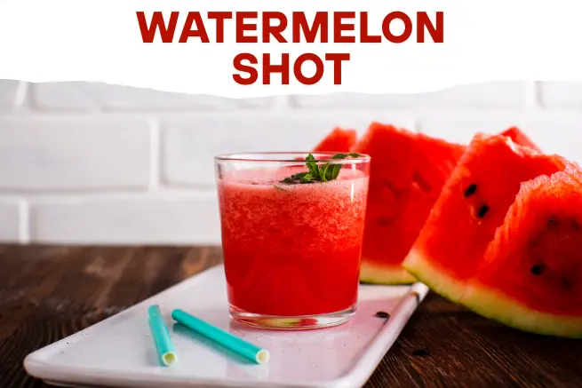 Refreshing watermelon shot in a clear glass garnished with mint, served with fresh watermelon slices on a white tray and wooden table background