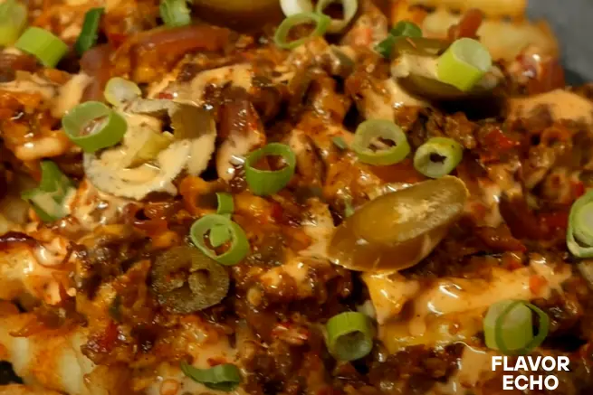 Close-up of loaded crinkle-cut papa locas fries topped with creamy sauce, seasoned ground beef, sliced jalapeños, and chopped green onions, highlighting the spicy and savory toppings
